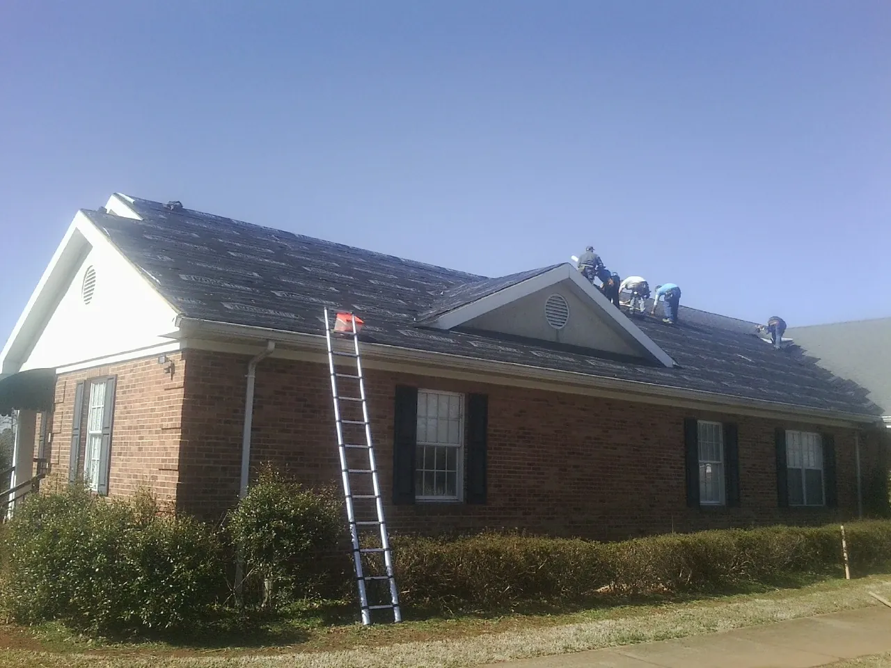 Crew tearing shingles off a brick ranch roof with a ladder set — Emergency Roof Repair work by our crew in Mount Tabor