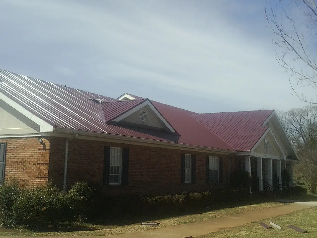 Red metal roof with gabled entries on a long brick building, from a Hail Damage Roof Repair job in Mount Tabor