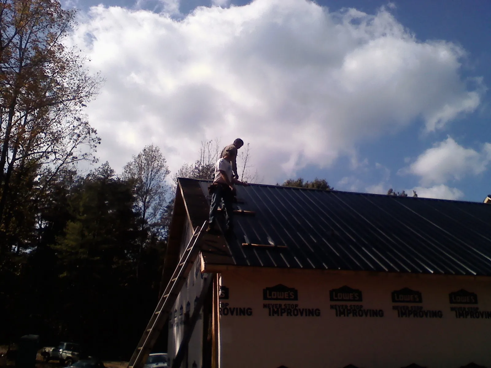 Roofer fastening dark metal panels high against a cloudy sky, from a Roof Inspection job in Mount Tabor