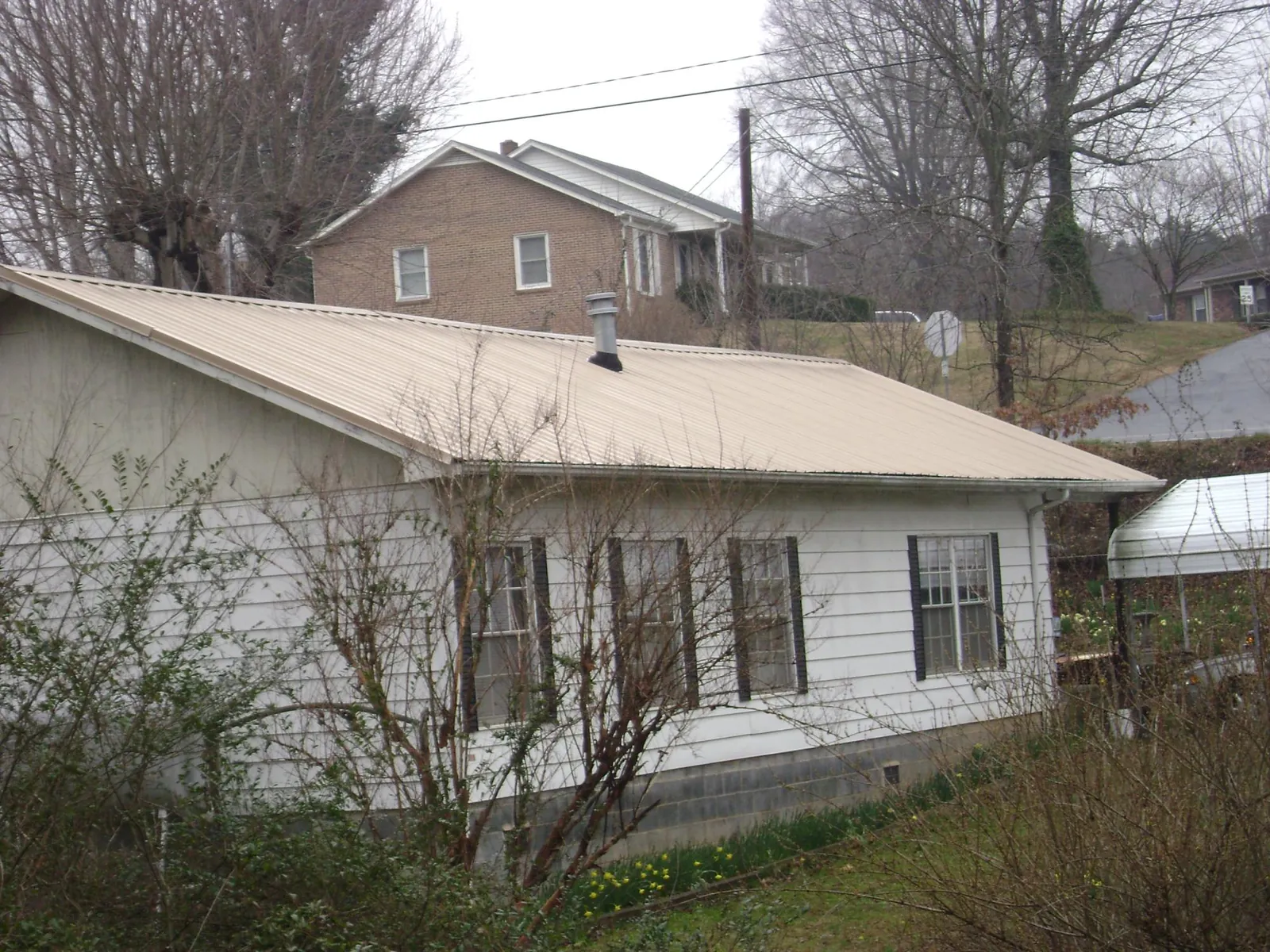 Tan metal roof on a white sided house set into a hillside — Commercial Roofing by Roofing Brothers in Mount Tabor