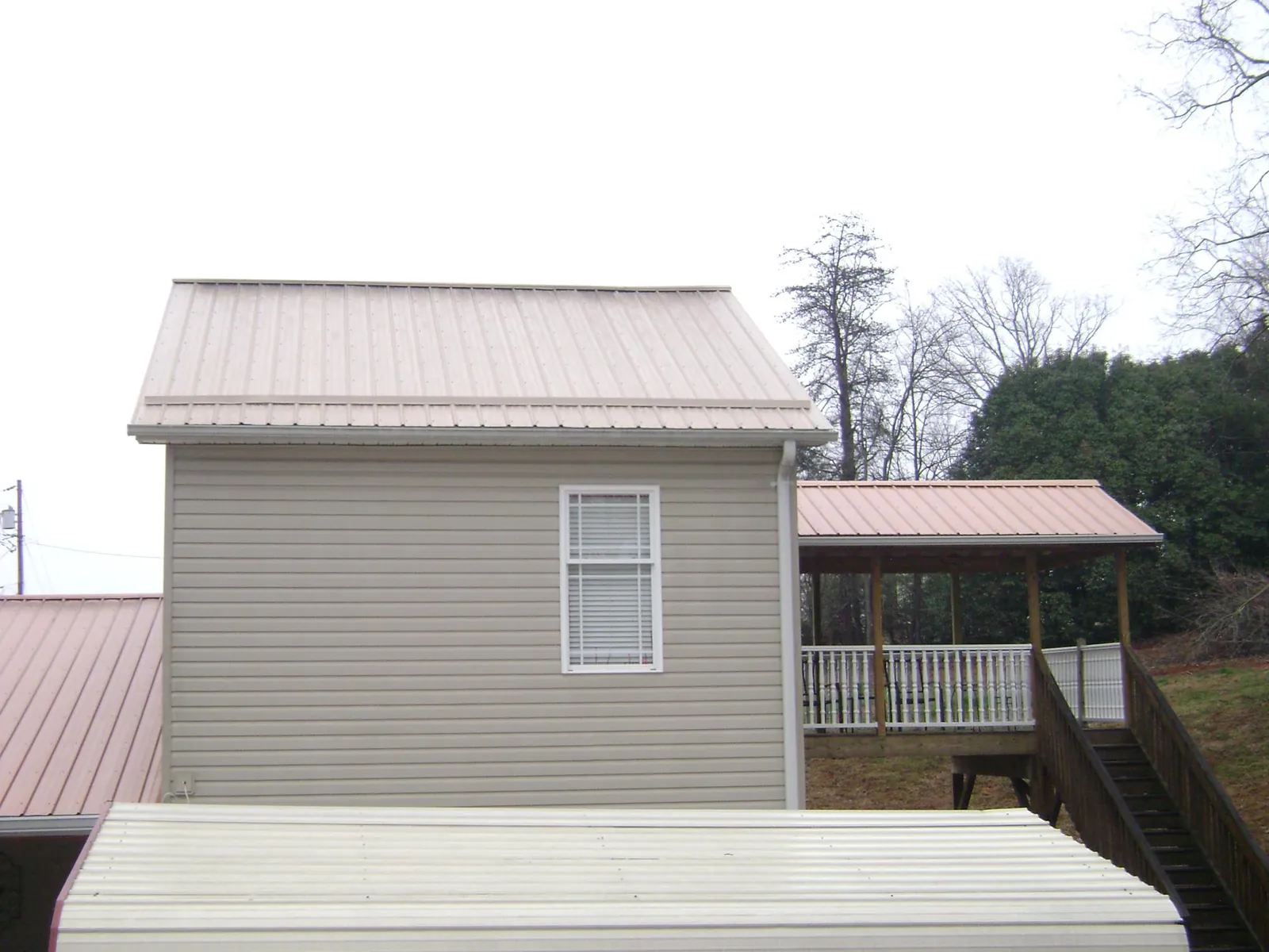 Tan metal roofs on a two story addition and attached porch, from a Roof Replacement job in Mount Tabor